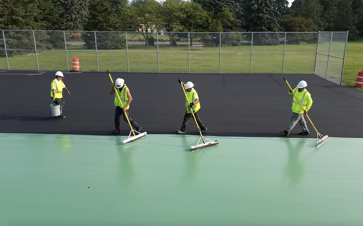 Workers applying green surface to sports court