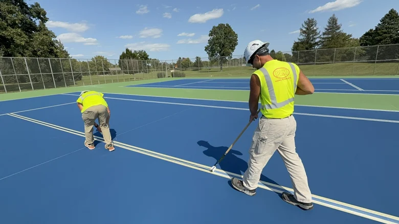 Workers painting lines on tennis court