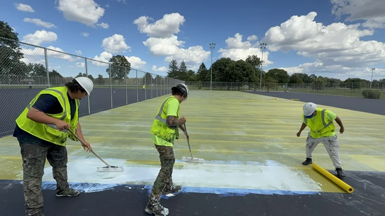 Workers painting a sports court surface.