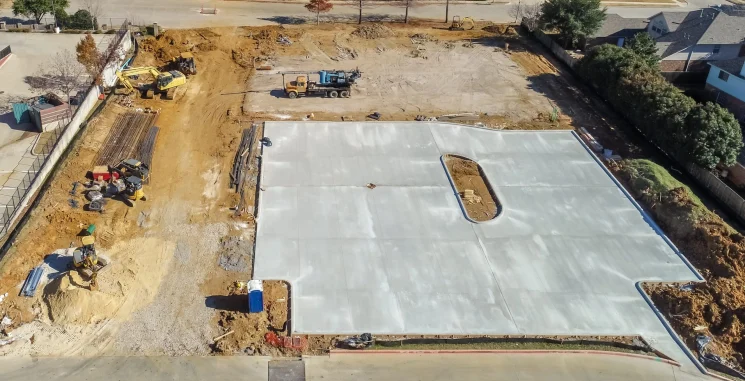 Aerial view of a newly poured concrete parking lot under construction with excavation equipment and work vehicles.