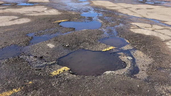 Pothole in parking lot filled with dirty water and road debris.